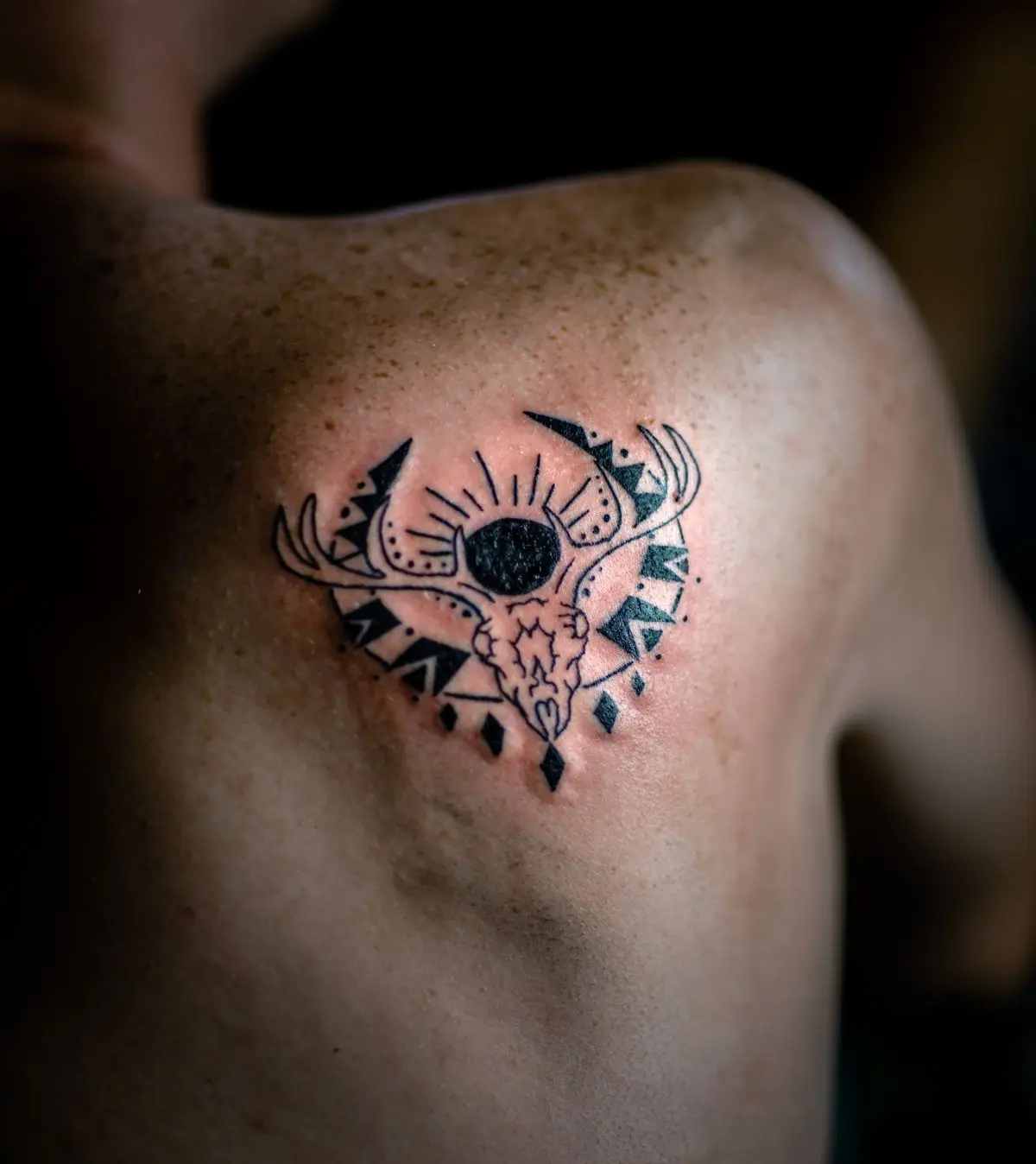 Small geometric blackwork piece with solid black fill and negative-space accents on the shoulder