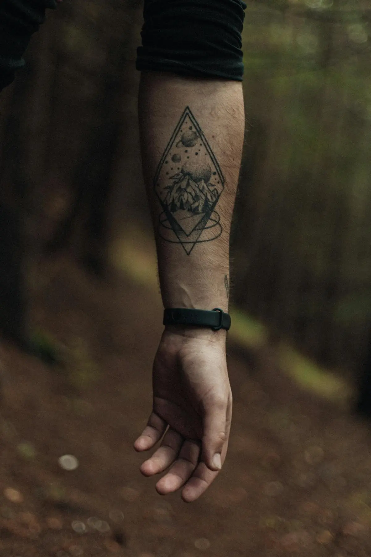Dotwork mountain and planets inside a rhombus frame on the forearm