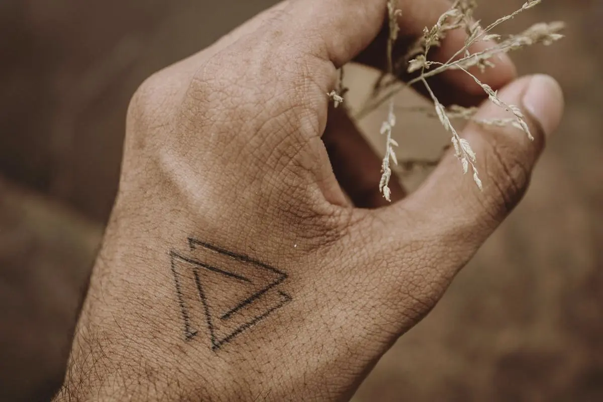 Two interlocking line triangles tattooed on the back of the hand