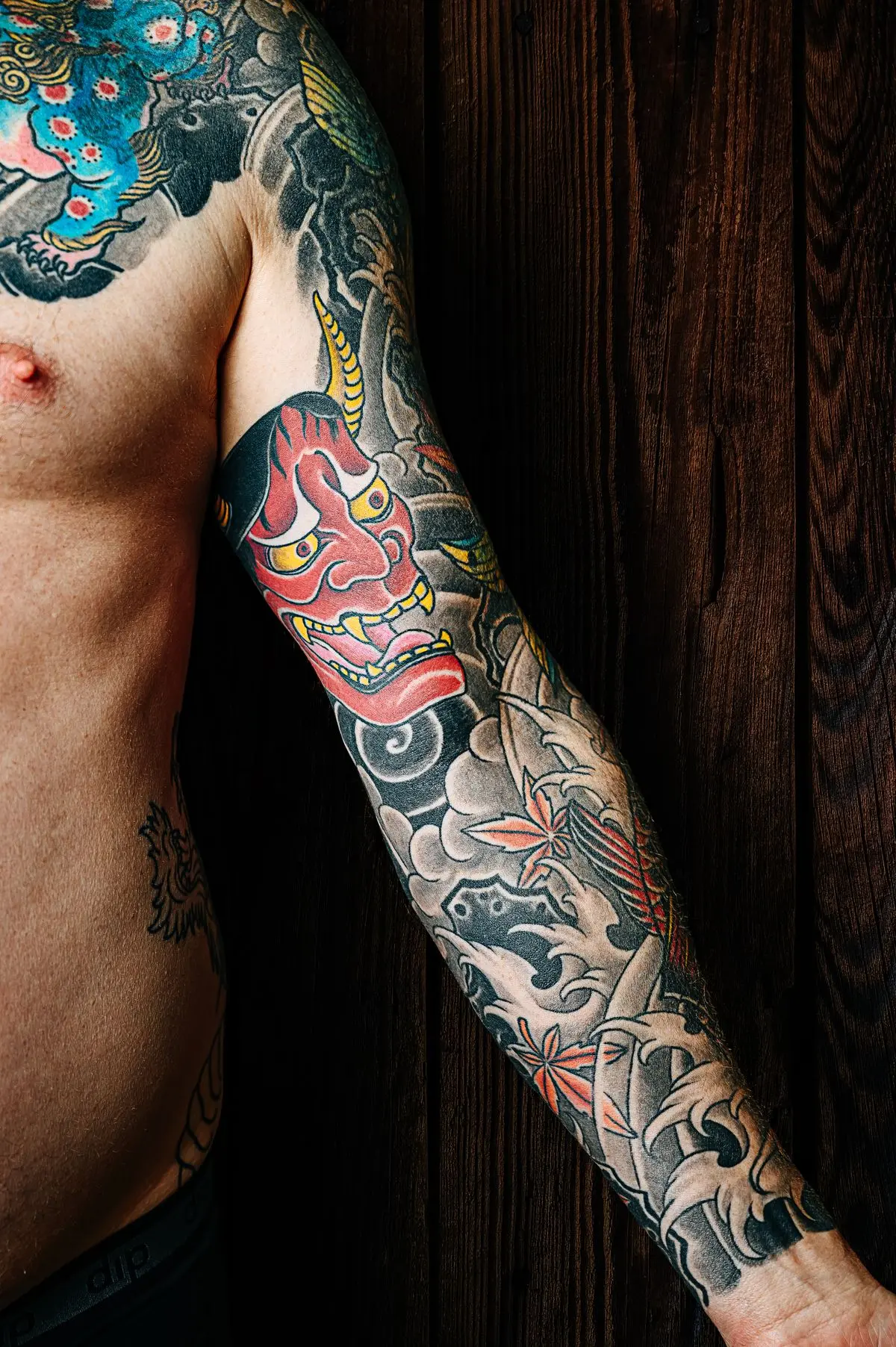 Double full sleeves with a green dragon, foo dog, and red koi over a bare chest