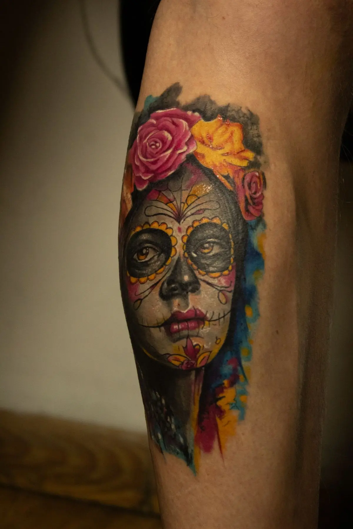 Día de los Muertos calf tattoo set against a blue and orange watercolor splash