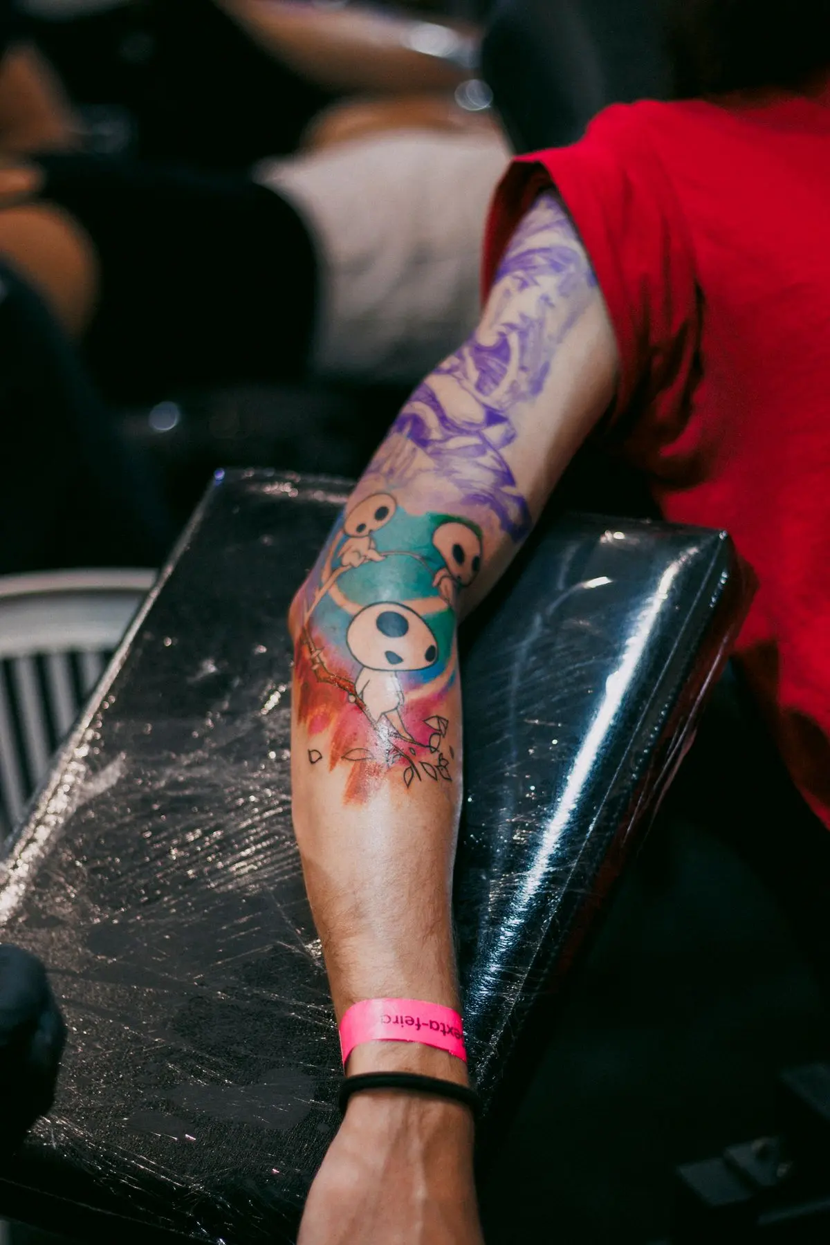 Watercolor forearm tattoo of spirit creatures over a colorful paint spray